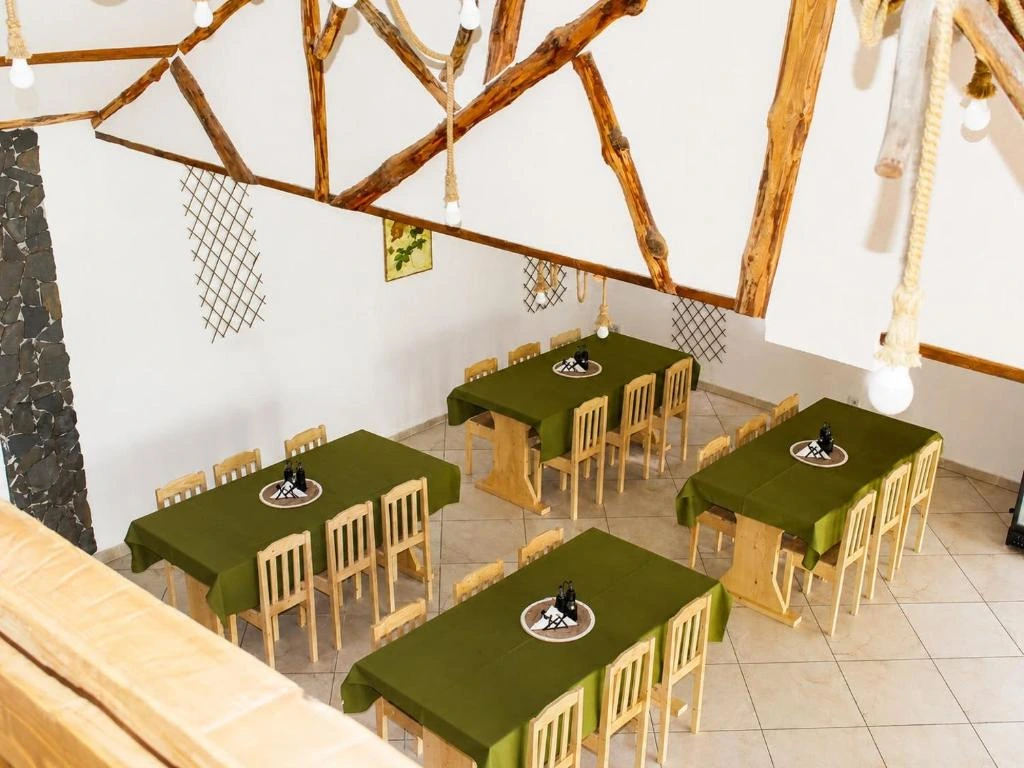Sala de mese a pensiunii cu piloni de piatră și fețe de masă verzi